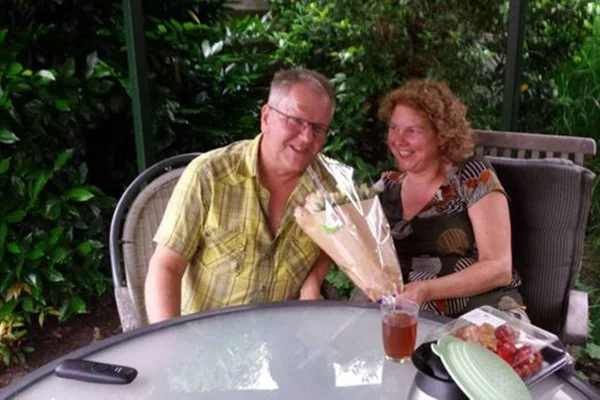 Imagem colorida de homem e mulher sentados a mesa com buquê de flores - Metrópoles