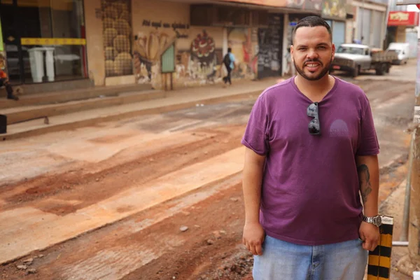 Empresário que ajudou em resgate a homem durante enxurrada no DF. Na foto, um homem com camiseta roxa e calça jeans está parado em uma rua - Metrópoles