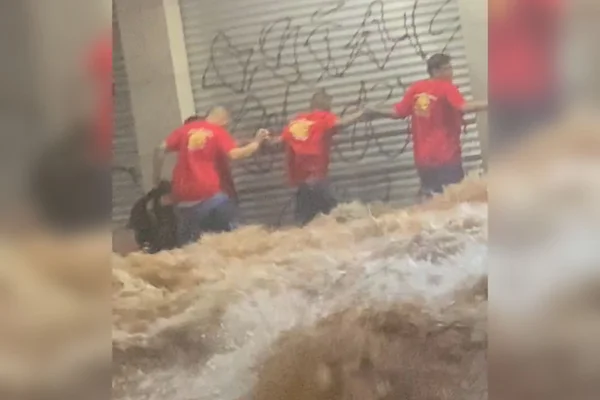 Imagem colorida de trabalhadores fazendo corrente humana para salvar homem de enchente no DF - Metrópoles