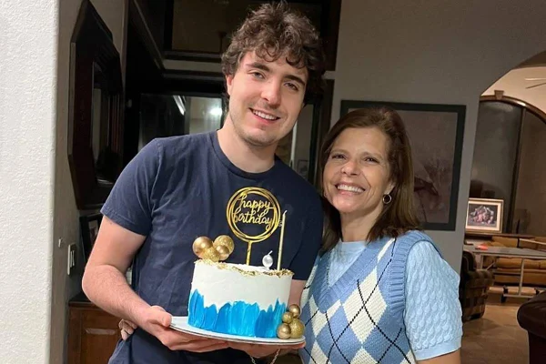 foto colorida de João Augusto Liberato, que veste uma blusa azul e segura um bolo decorado em branco e azul, e a mãe, Rose Miriam, também vestida de azul - metrópoles