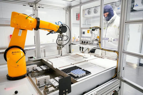6 de fevereiro de 2024, Baden-Württemberg, Mannheim: Um funcionário está diante de um robô que etiqueta frascos com o ingrediente ativo do produto Elevidys para o tratamento da distrofia muscular de Duchenne na fábrica da Roche Diagnostics GmbH. A coletiva de imprensa anual da Roche Pharma foi realizada hoje. Foto: Uwe Anspach/dpa (Foto de Uwe Anspach/picture alliance via Getty Images)