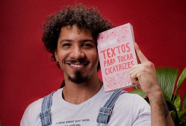Igor Pires de macacão mostrando a capa do livro Para Tocar Cicatrizes