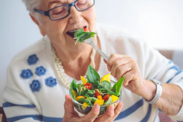 Foto colorida de mulher comendo verduras. Ela segura uma tigela com verduras e legumes - Metrópoles