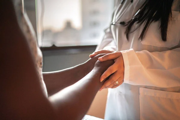 Medica segurando mãos de paciente para falar