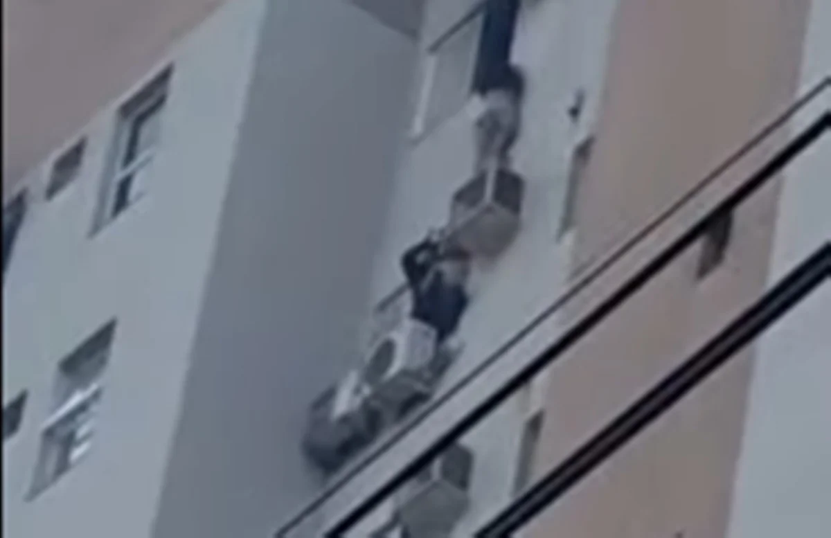 Imagem colorida do momento em que mulher se pendura em ar condicionado