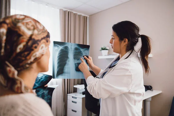Paciente sentada na maca vê médica apresentando raio-x de seu toráx