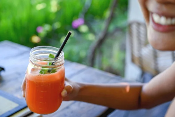 Mulher sorridente segurando suco de cenoura espremido na hora. Suco para emagrecimento.