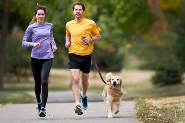 Imagem colorida de casal correndo com golden retriever