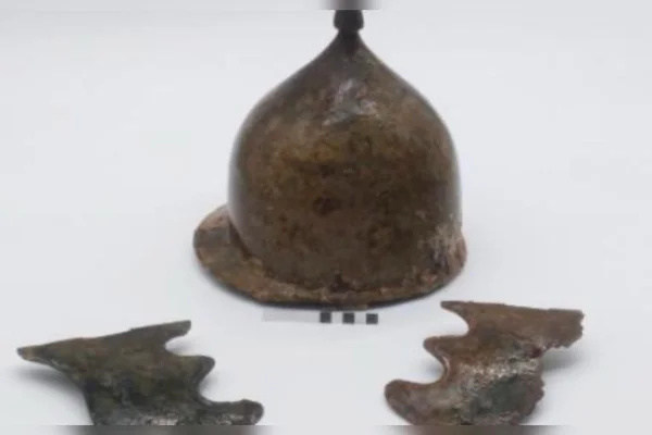 Foto colorida de capacete antigo de bronzo sobre uma superfície branca - Metrópoles