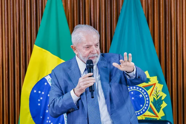 Presidente Lula no Palácio do Planalto, em frente à bandeira do Brasil, com microfone e mão estendida - Metrópoles