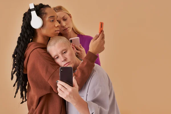 Foto colorida de meninas apoiadas umas nas outras enquanto estão com celular na mão