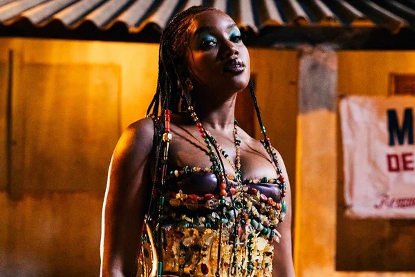 Imagem colorida da cantora IZA. Ela está com uma roupa colorida, é negra e tem o cabelo preto - Metrópoles