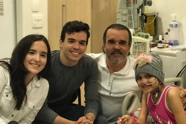 Foto colorida de pai com três filhos no hospital, uma delas diagnosticada com câncer em hospital - Metrópoles