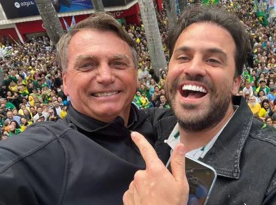 Selfie de dois homens de preto com público ao fundo
