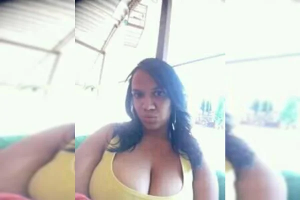 Mulher de cabelos morenos longos olha para foto. Ela veste blusa amarela