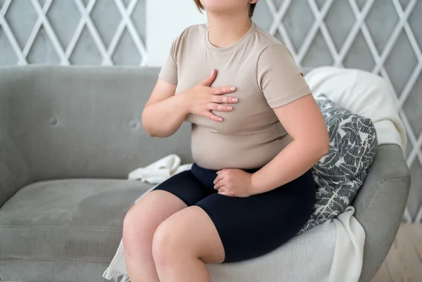 Foto colorida de mulher sentada em sofá com mão no coração - Metrópoles