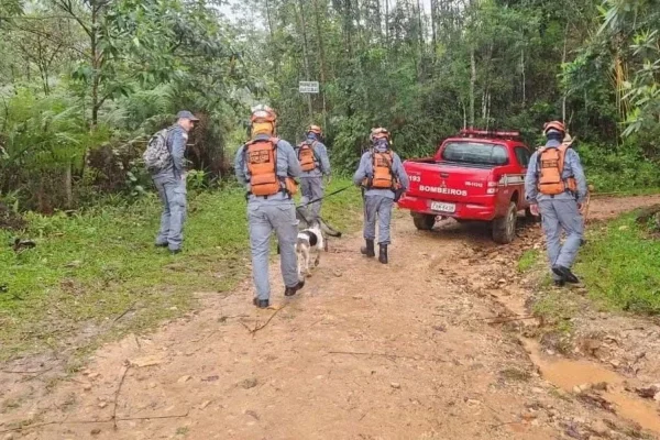 Imagem colorida de Corpo de Bombeiros realizando buscas a um homem em trilha com lama e mata fechada. Metrópoles