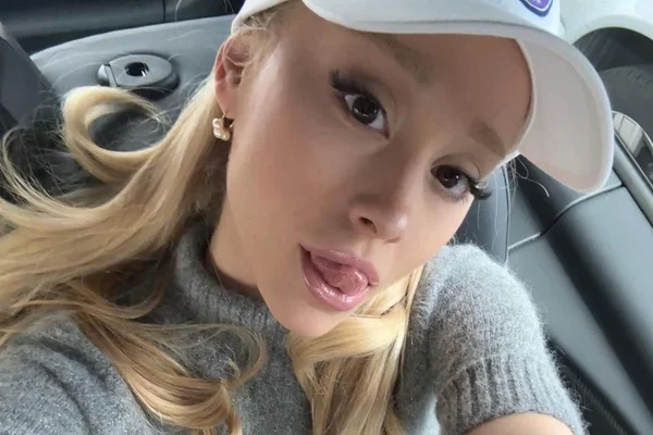 Foto colorida de Ariana Grande. A cantora está com um boné branco, um sueter claro, é branca e loira - Metrópoles