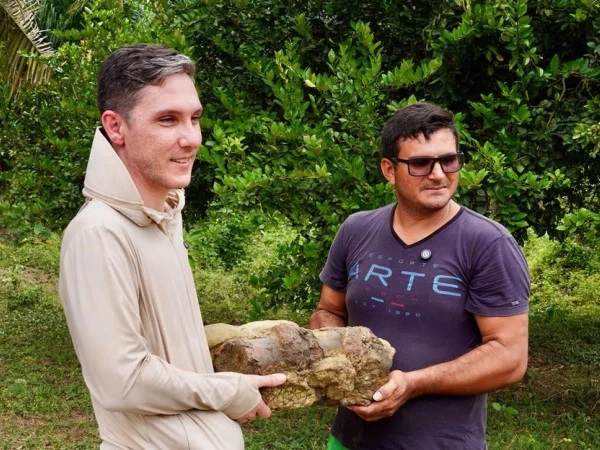 Foto colorida de dois homens segurando fóssil - Metrópoles