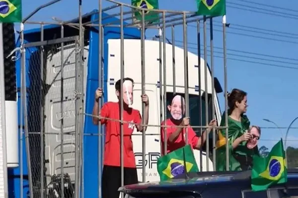 Foto mostra crianças com máscaras do presidente eleito Lula e do ministro do STF, Alexandre de Moraes, presas em jaulas sob caminhão em manifestação bolsonarista, na cidade de Balenário Camboriu (SC). Várias bandeiras do Brasil adornam o local - Metrópoles