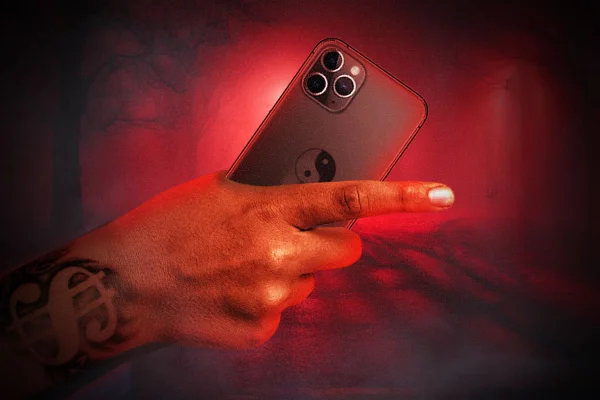 Arte gráfica de mão segurando celular, com fundo infernal vermelho - Metrópoles
