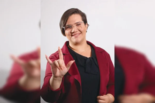Mulher fazendo sinal em Libras com camisa preta e blazer vinho