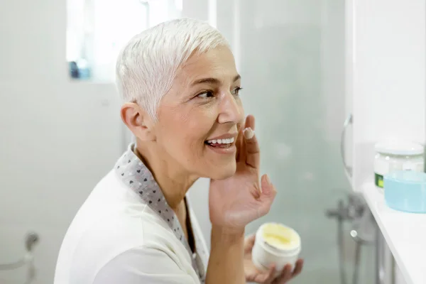Foto colorida de uma mulher passando creme no rosto - Metrópoles