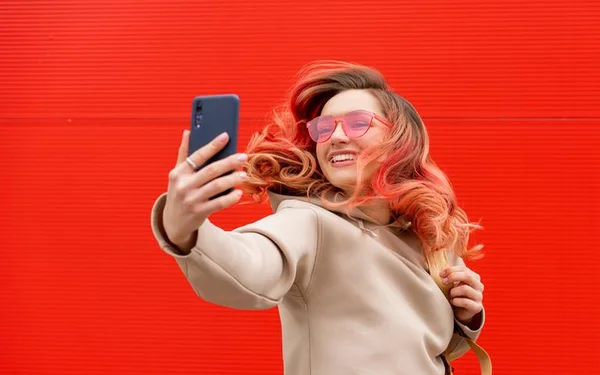 Mulher segurando celular em frente ao rosto em um fundo vermelho