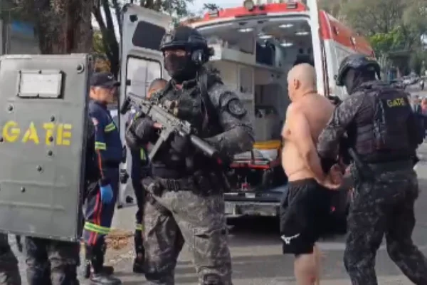 Imagem colorida de homem sem camisa, preso pelo Gate, sendo levado à uma ambulância. Metrópole