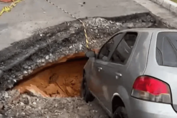 Imagem colorida de um carro prata engolido por um buraco na via - Metrópoles