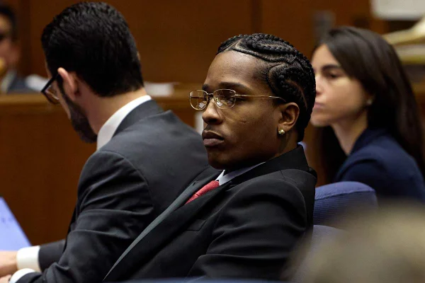 A imagem mostra o rapper Asap Rocky sentado dentro de um tribunal. Com feição séria, o artista olha para frente usando óculos de grau