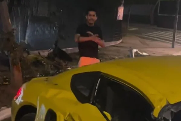 Imagem colorida de homem pardo, de camiseta preta e bermuda salmão, perto de Porsche amarelo, em rua, no período noturno - Metrópoles