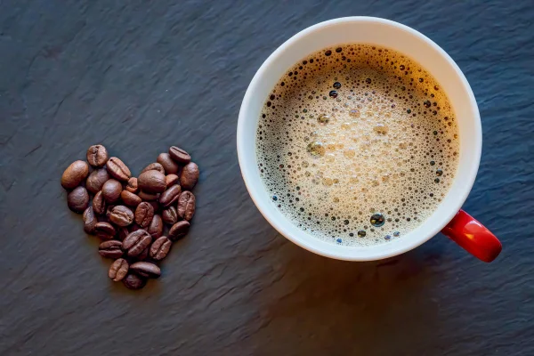 Foto colorida de xícara de chá e grãos de café que formam um coração - Metrópoles