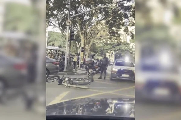 Imagem colorida de um motociclista caído na rua após colidir com um carro prata - Metrópoles