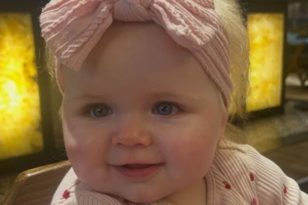 Foto colorida de uma bebê de olhos azuis, vestiva de rosa claro - Metrópoles.
