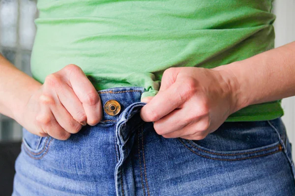 Mulher tenta fechar botão de calça jeans - Metrópoles