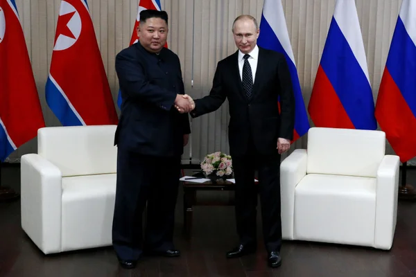 Imagem colorida mostra Kim Jong-un e Putin apertando as mãos em frente as bandeiras da Coreia do Norte e da Rússia - Metrópoles