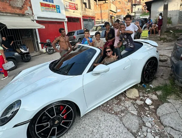 Foto colorida mostra influenciador Maykon Santos em Porsche branca rodeado por crianças