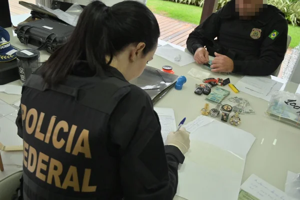 Imagem colorida de apreensões da PF em casa de homem prourado pela Interpol