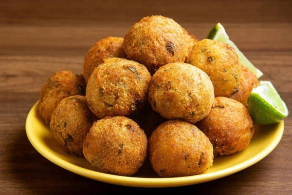 Na foto temos um prato amarelo com varios bolinhos redondos e duas fatias de limão