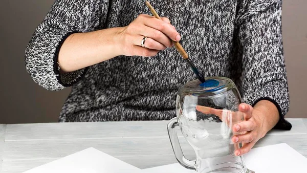 Mão feminina pintando jarro de vidro com tinta azul - Metrópoles
