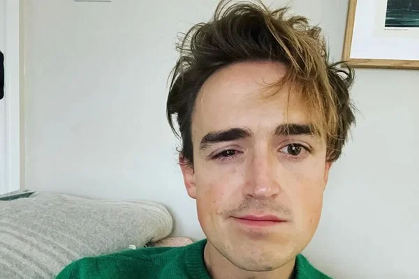 Tom Fletcher. Ele tem pele clara, cabelo castanho com mechas loiras, está com um problema ocular e usa camisa verde - Metrópoles