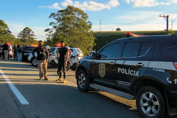 Foto colorida de policiais parados em frente a viatura da Polícia Civil, em Campos do Jordão, interior de São Paulo.