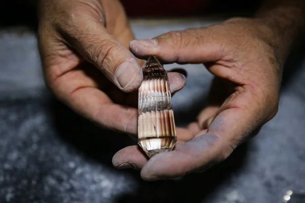 Imagem colorida das mãos de um homem lapidando uma pedra de cristal