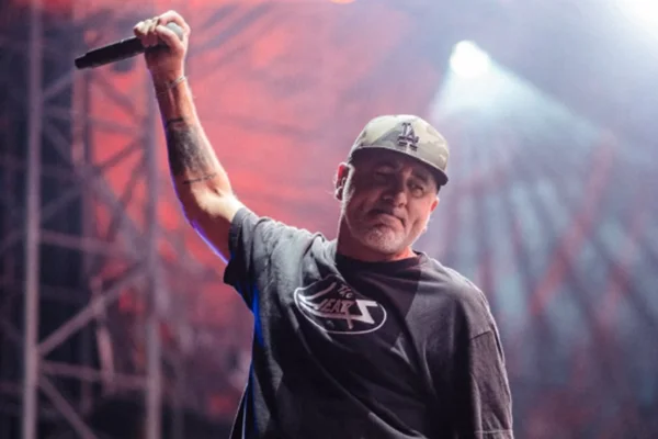 Foto do vocalista da banda Pennywise. Ele usa um boné e segura um microfone no palco de um show - Metrópoles