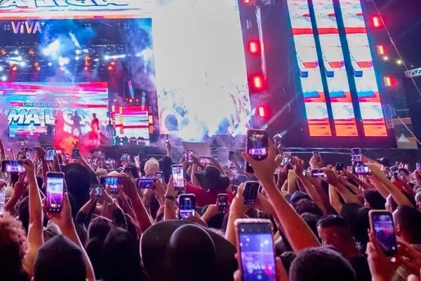 Imagem colorida mostra multidão com os braços para cima em frente a palco onde acontece shpw de música - Metrópoles