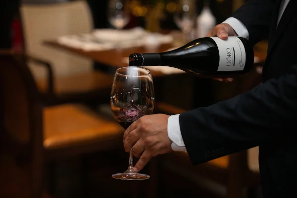 Na foto, um homem serve vinho em uma taça - Metrópoles