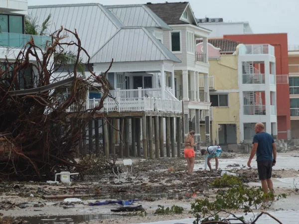 Foto colorida de pessoas caminhando entre árvores caídas e detritos em praia na Flórida, deixados pela passagem do furacão Helene - Metrópoles