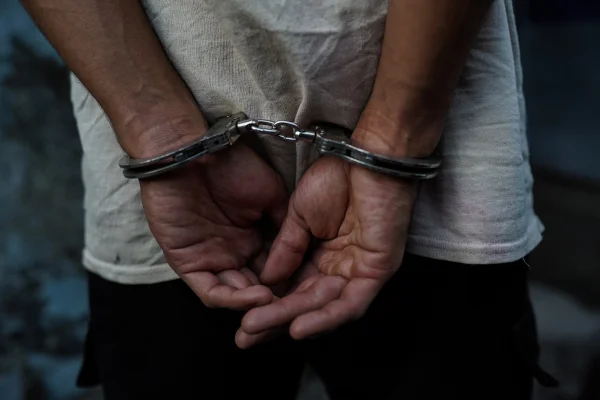Imagem colorida de homem com algemas. Suspeito é preso por tentativa de feminicídio, ateando fogo no corpo da companheira. - Metrópoles