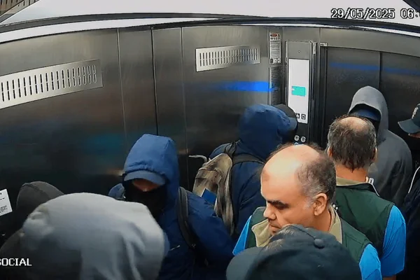 Imagem colorida de homens encapuzados rendendo outro homem em um elevador social - Metrópoles